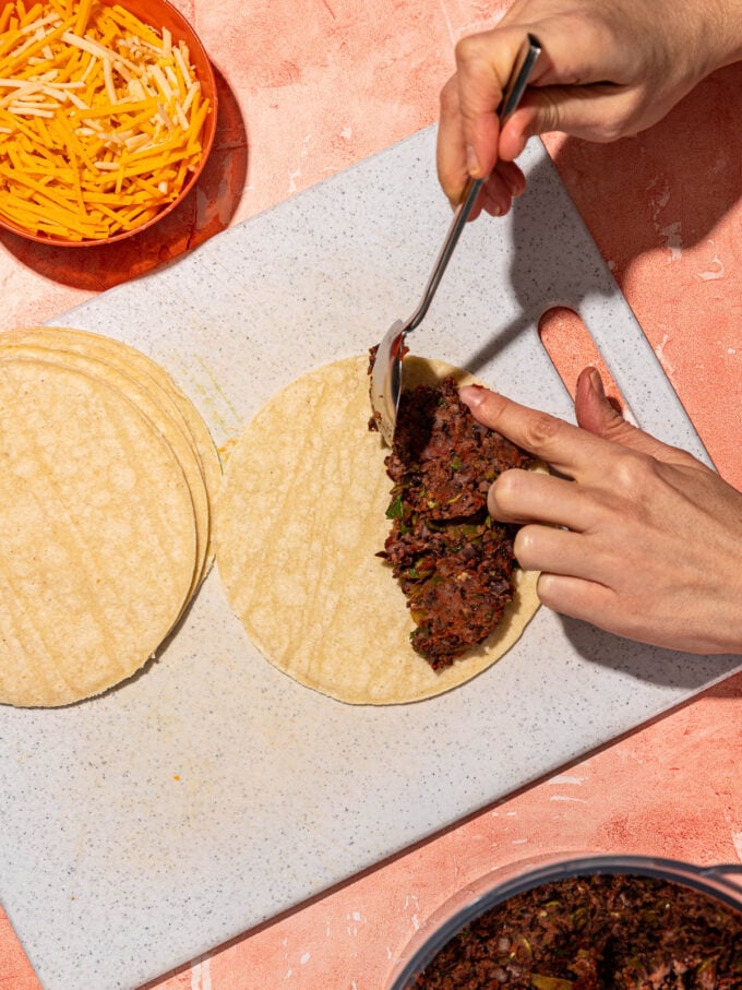 hand scooping smashed black beans onto tortilla