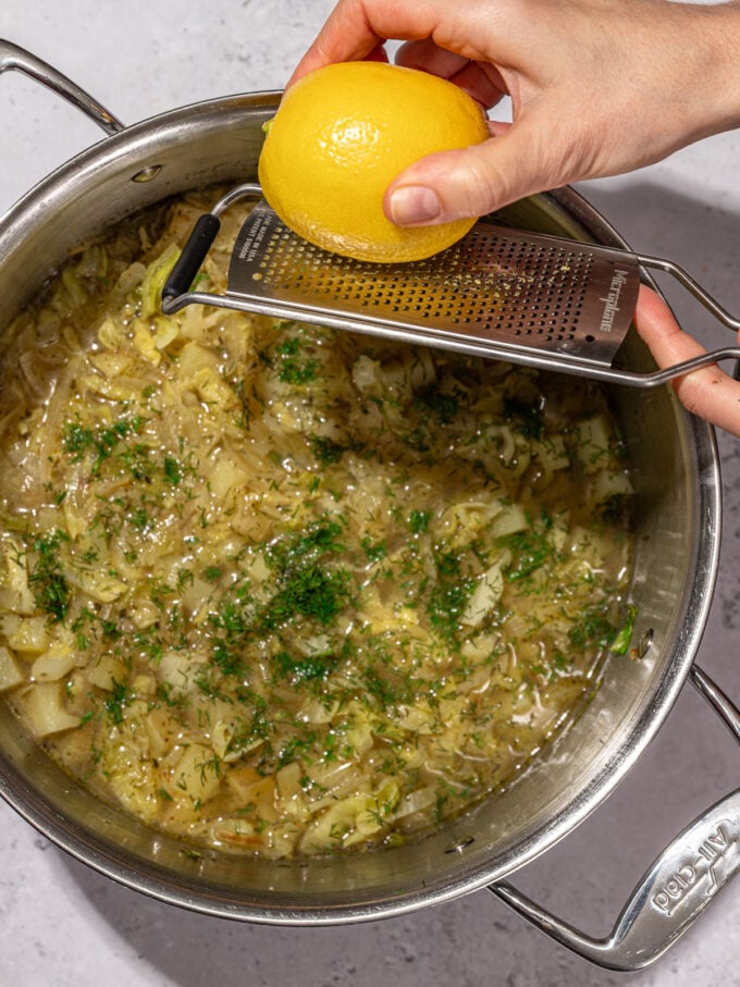 hand zesting lemon into pot of cabbage soup