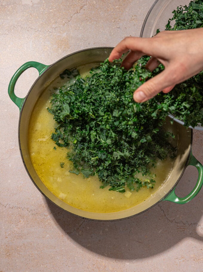 hand adding kale to soup