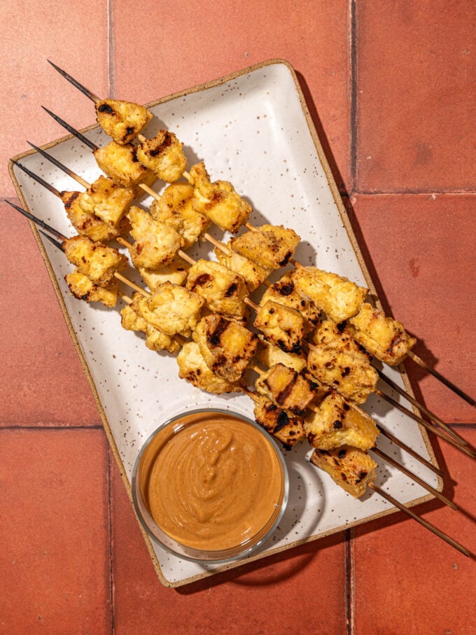 tofu skewers on white plate with peanut sauce