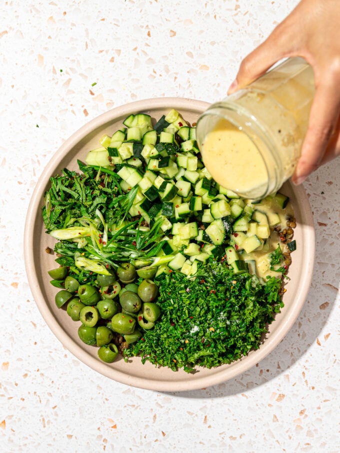 hand pouring dressing over a lentil salad