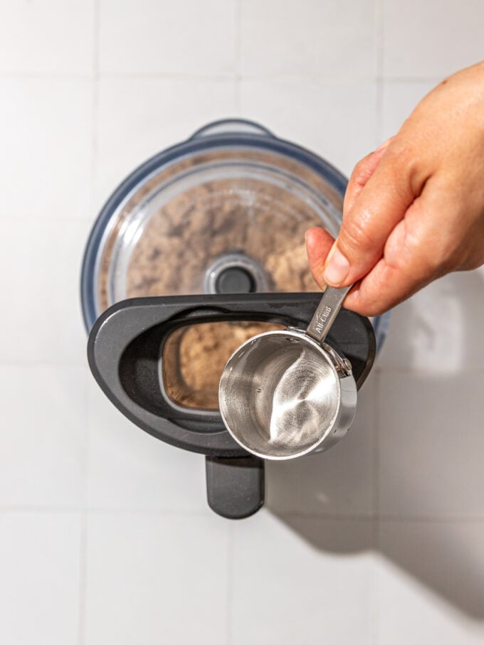 hand pouring water into food processor