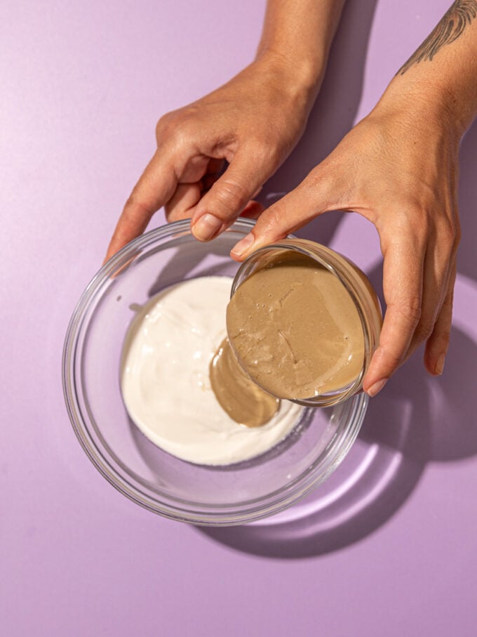 hand pouring tahini into yogurt