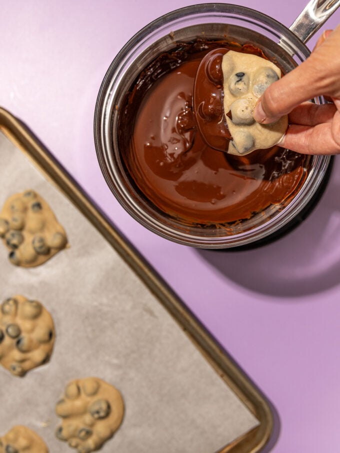 hand dunking yogurt cluster into chocolate