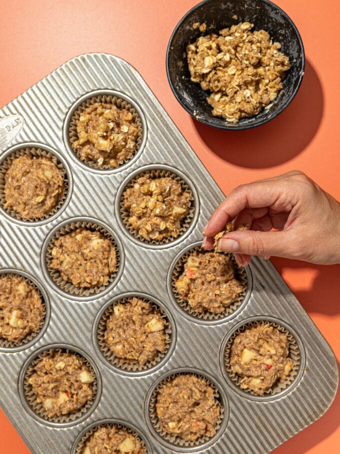 hand crumbling topping onto apple muffins