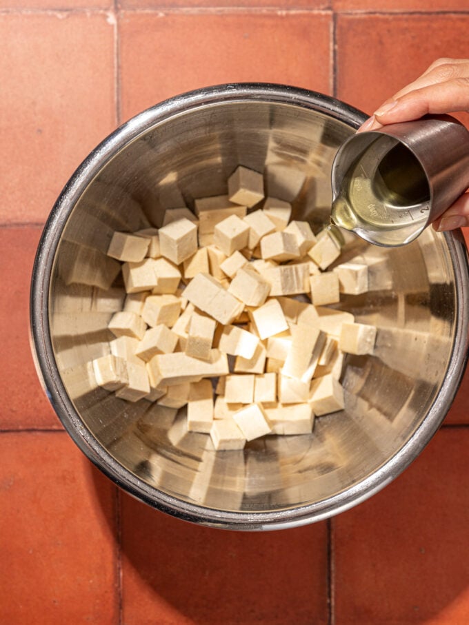 hand pouring oil over tofu