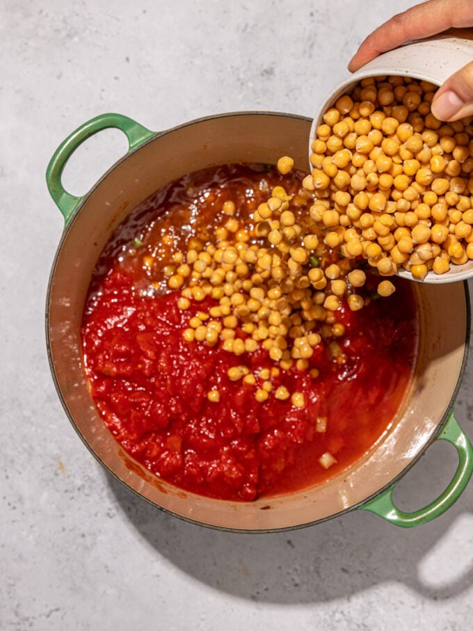 hand pouring chickpeas into stew