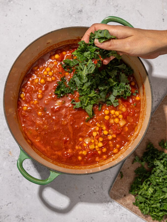 hand adding kale to stew