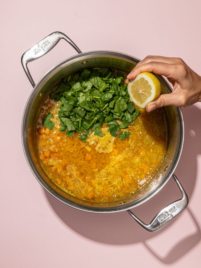 hand squeezing lemon into lentil soup