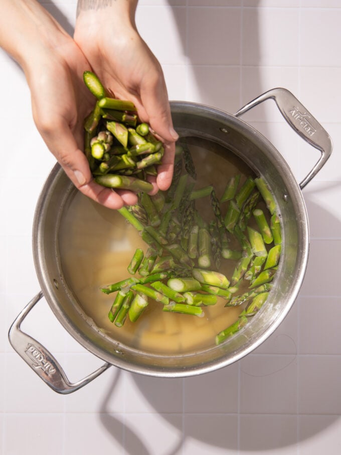 hand dropping asparagus into pasta pot