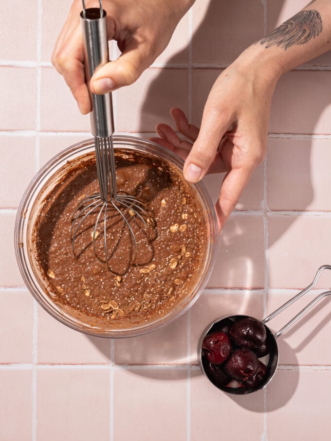 hand whisking chocolate oats with cup of cherries