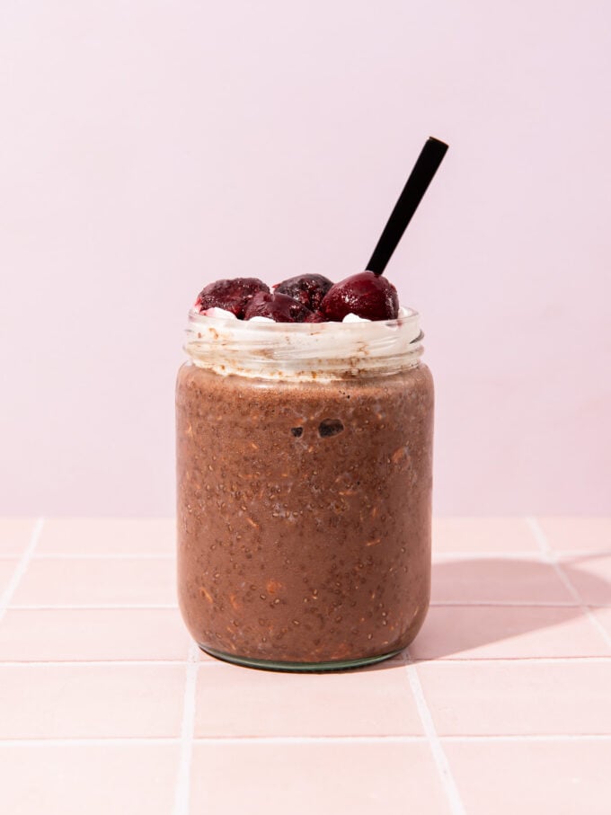 chocolate overnight oats with cream and cherries in jar with spoon