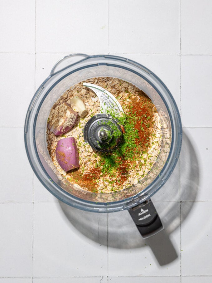 oats, lime zest, cumin and shallot in a food processor on white background