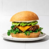 burger and bun on white plate with avocado and cheese