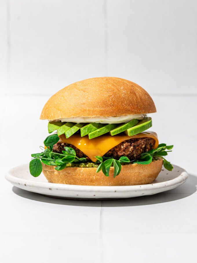 burger and bun on white plate with avocado and cheese