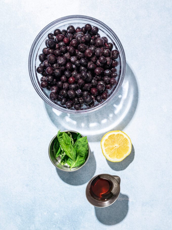 glass bowl of blueberries with basil, lemon and maple syrup on blue background