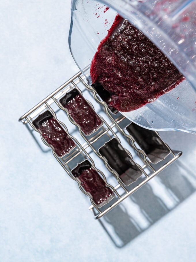 pouring blueberry mix from a blender into popsicle molds