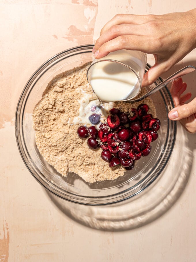 hand pouring milk into glass bowl with cherries and flour