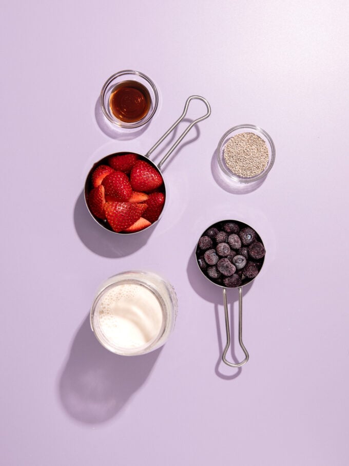 strawberries, blueberries, milk and chia seeds in cups on purple background