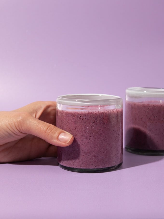 hand holding glass of berry smoothie on purple background