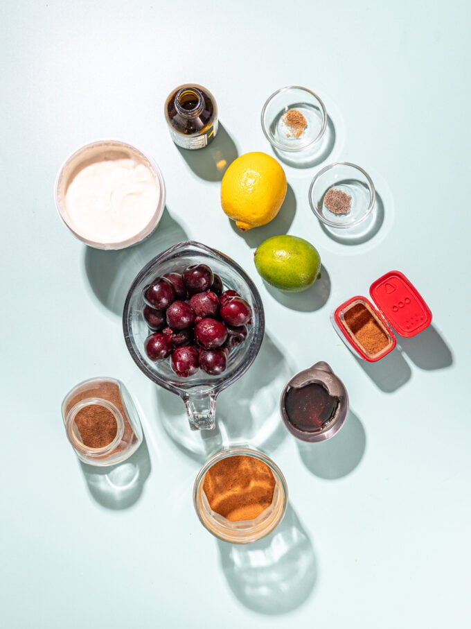 bowl of cherries, yogurt, a lemon and lime and bowls of spices on blue background