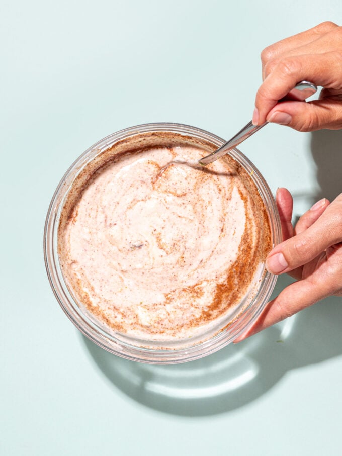 hand stirring spices into bowl of yogurt