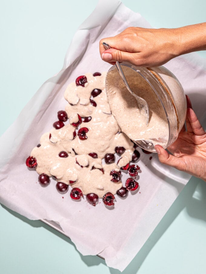 hand pouring yogurt onto cherries on baking sheet