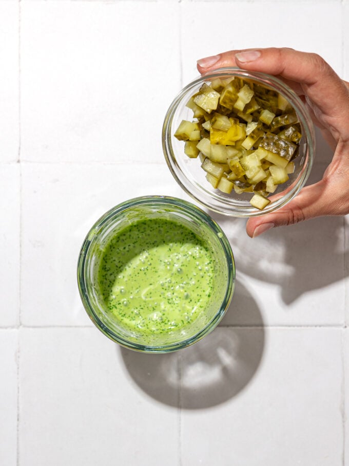 hand pouring pickles into green sauce