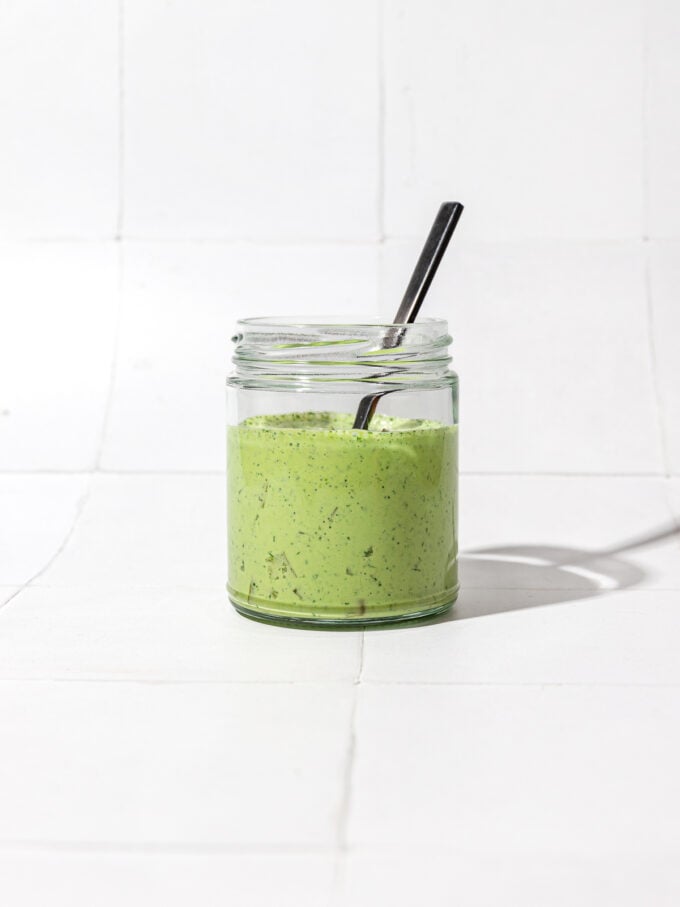 creamy green dressing in glass jar with black spoon