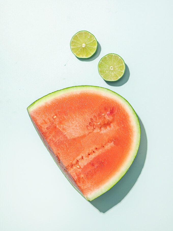 piece of watermelon and sliced lime on blue background