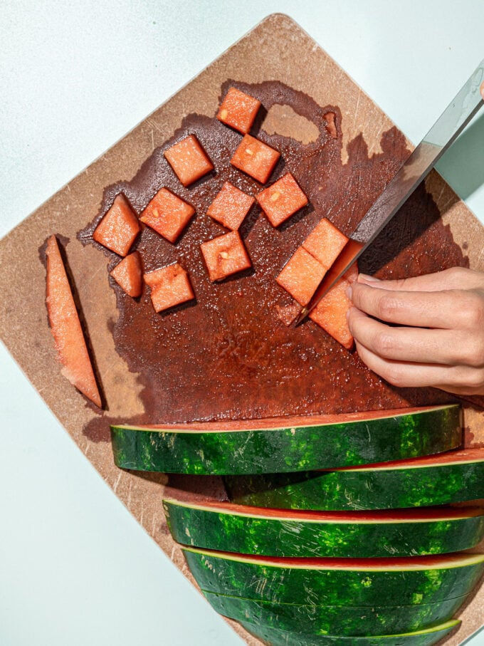 hand slicing watermelon into cubes on cutting board