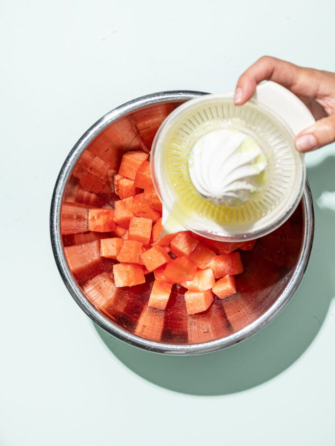 hand pouring citrus juice into bowl of watermelon