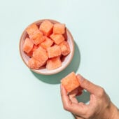hand holding frozen watermelon chunk beside white bowl with watermelon