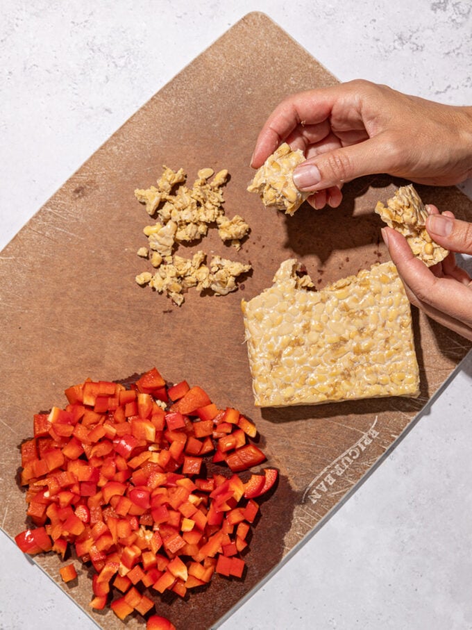 hand crumbling tempeh with red pepper on cutting board