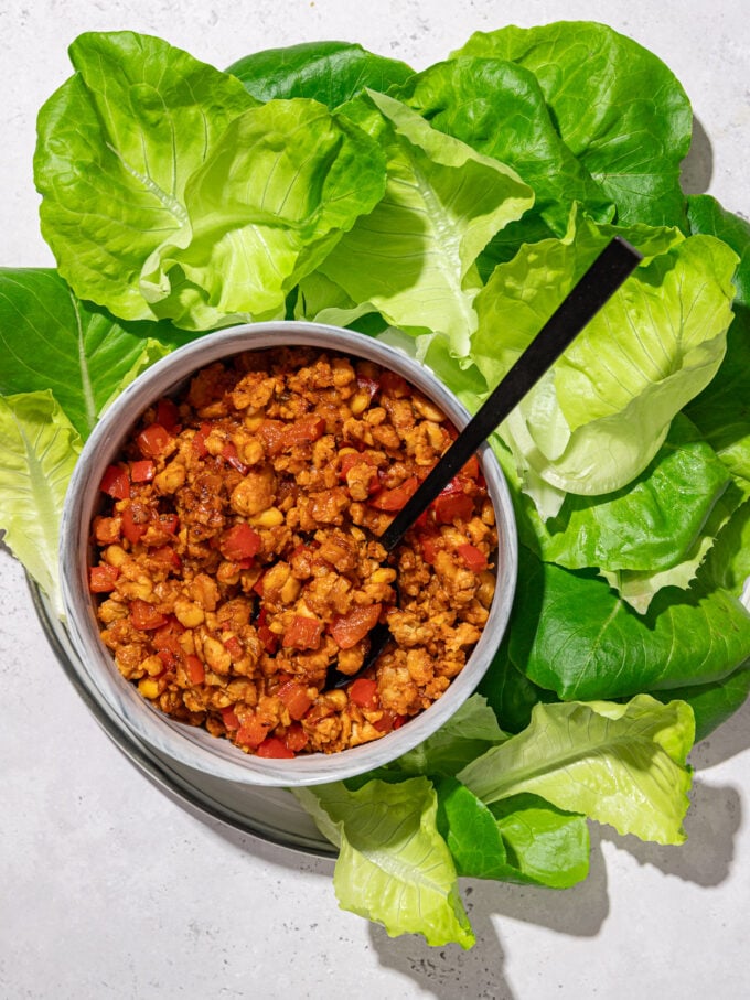 crumbled tempeh in bowl with black spoon and lettuce leaves
