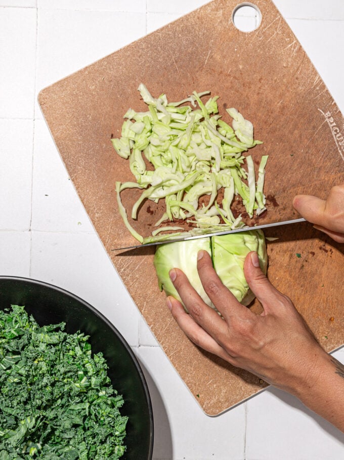 hand shredding green cabbage with knife on wood cutting board