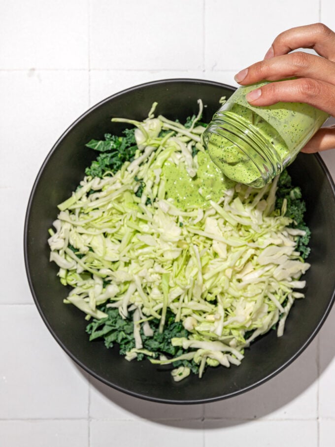 hand pouring green dressing on to kale and cabbage salad 