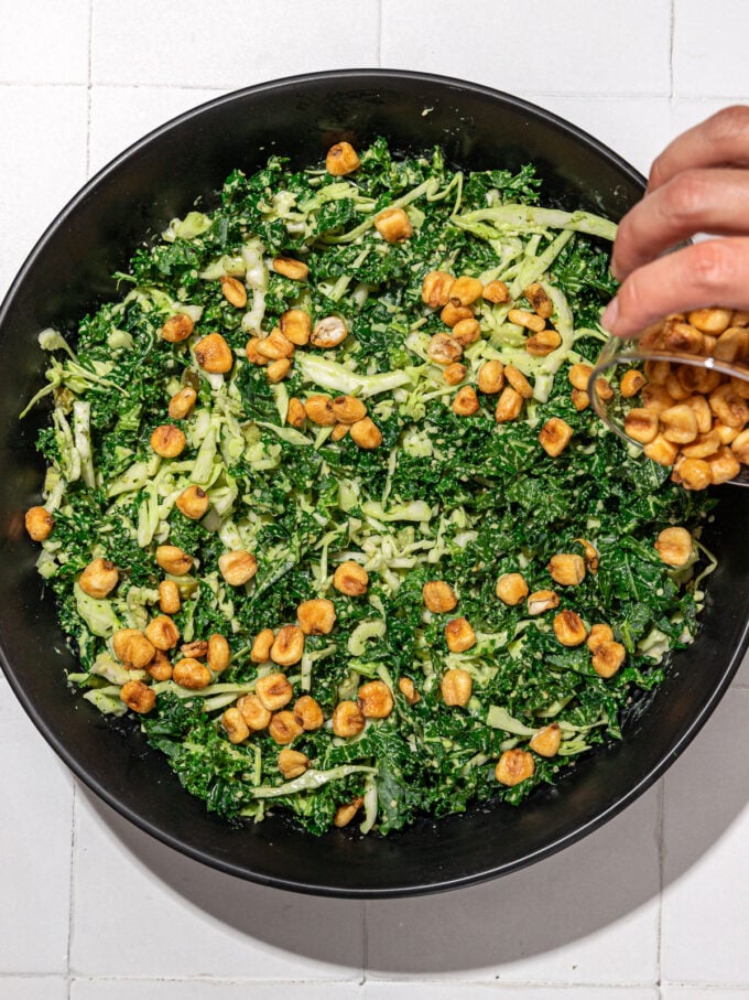 hand sprinkling corn nuts on kale and cabbage salad