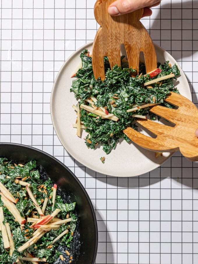 placing kale apple salad on white plate with wooden scoops
