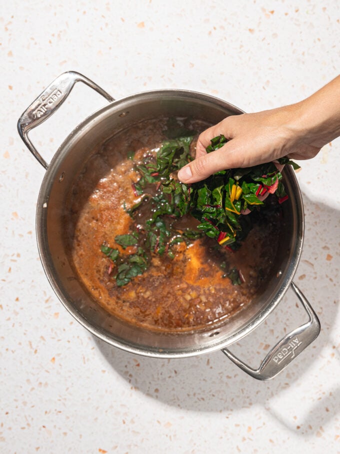 hand adding swiss chard to black bean soup