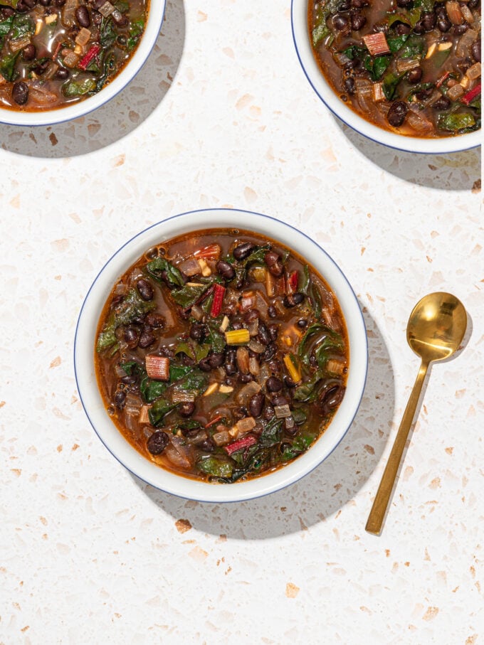 white bowls of black bean and swiss chard soup with gold spoon