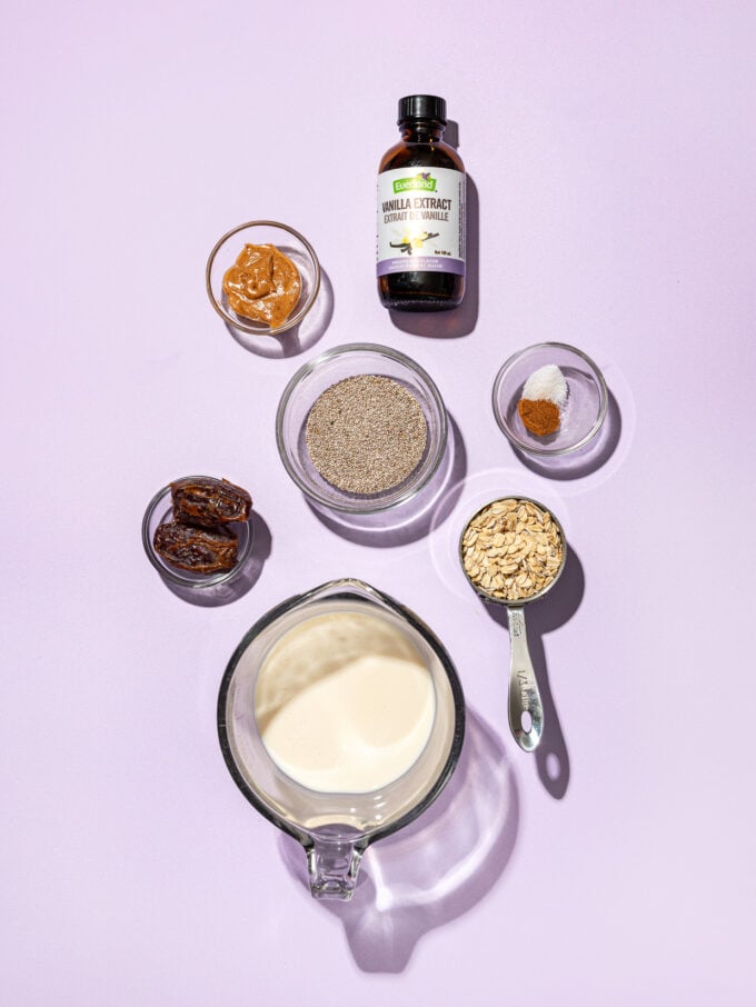 bowls of milk, oats, chia seeds and dates on purple background