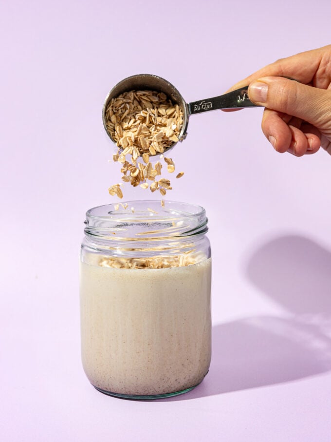 hand pouring oats into jar of milk