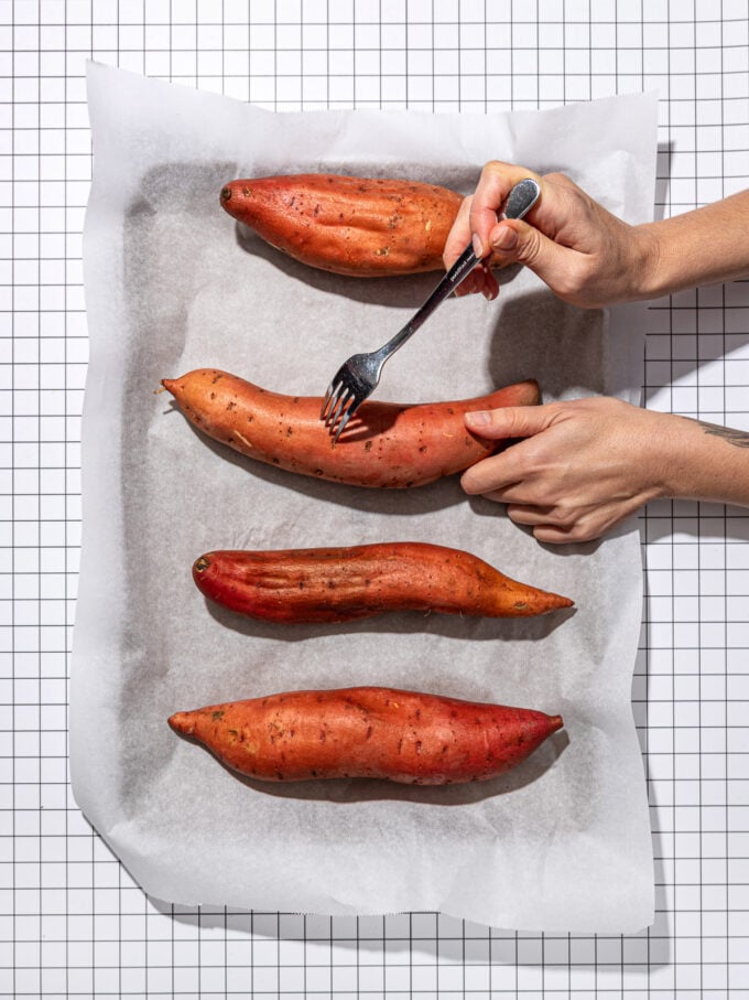 hand piercing sweet potatoes with a fork