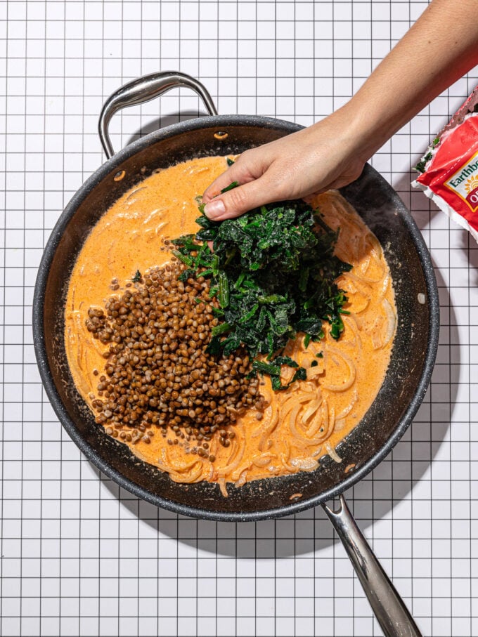 hand adding spinach to curry lentils