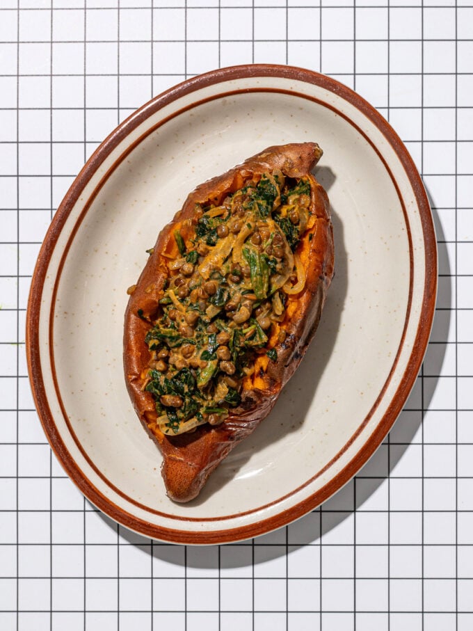 sweet potato stuffed with lentils and spinach on a brown edged oblong plate
