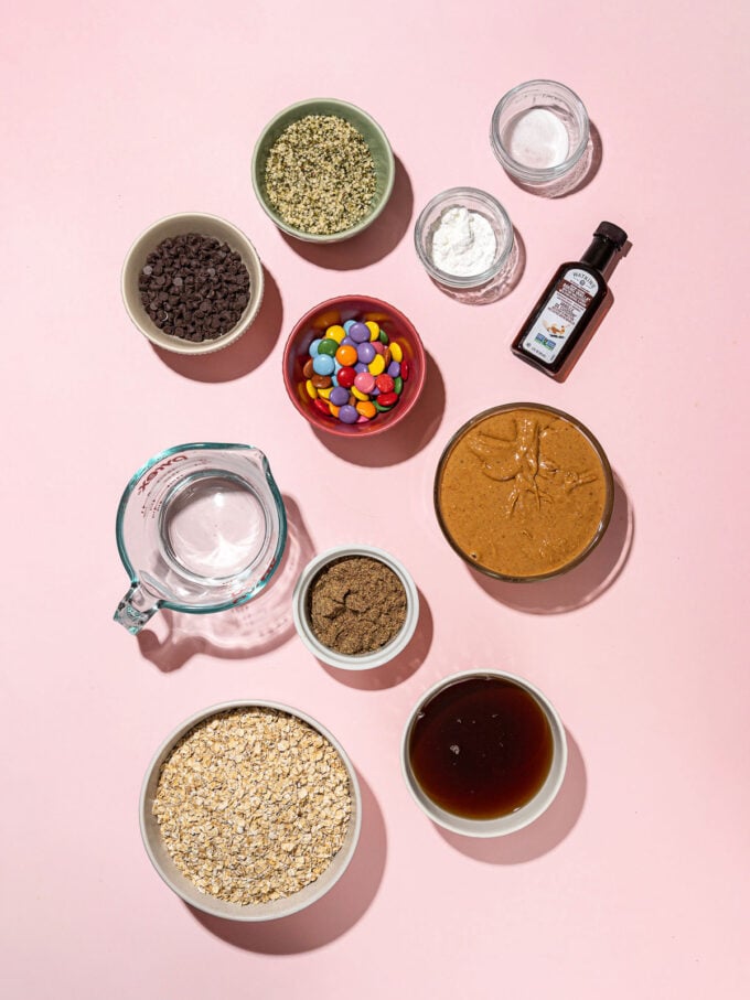 bowls of hemp hearts, rolled oats, peanut butter and candies on pink background