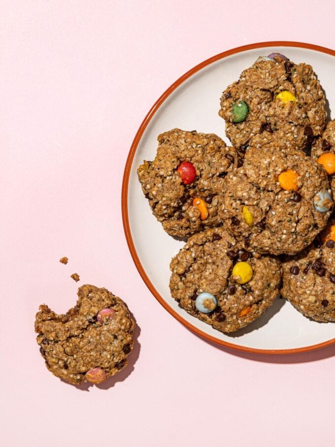 vegan monster cookies piled on a white plate with one cookie to the side missing a bite 