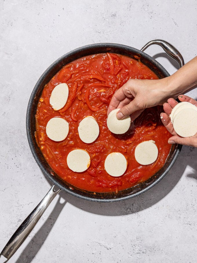 hand adding slices of silken tofu to shakshuka skillet