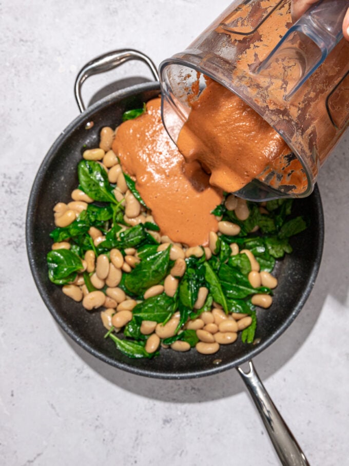 pouring rose sauce out of a blender onto a skillet with butter beans and spinach
